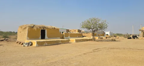 An earthen dwelling and tree beneath a clear sky